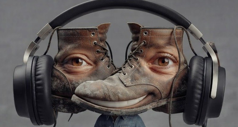 Timmus Shoes up close: his head is a pair of old scuffed brown work boots side by side, a warm brown eye on each boot, the right boot's toe curled up into a wide smile, and big black headphones around both boots